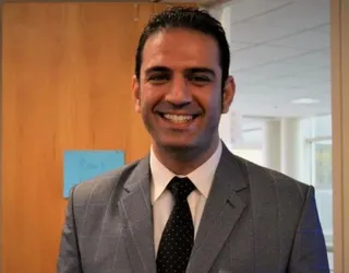 Mahmoud Abdi Tabari, smiling, in a grey suit at the door of his office